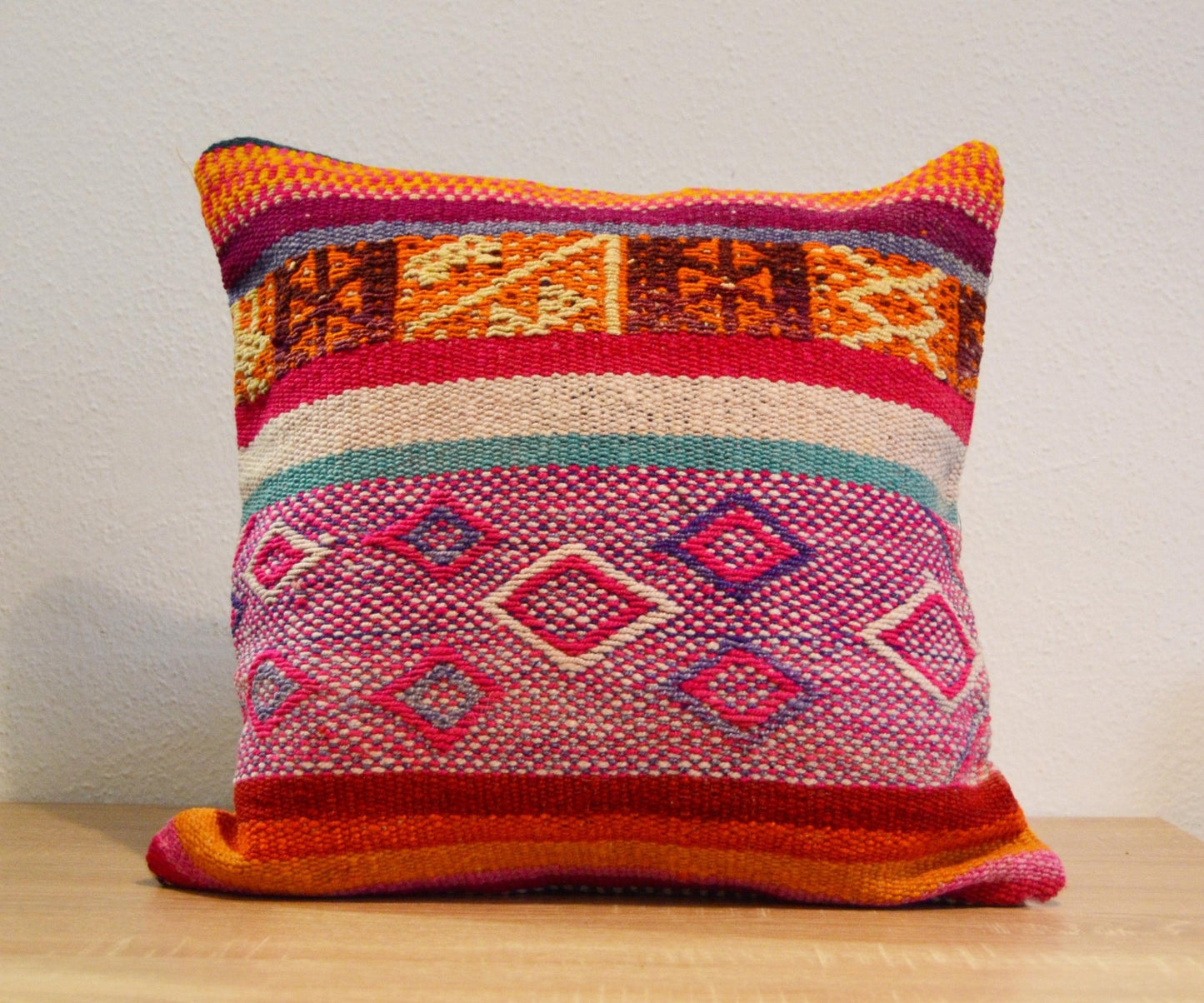 Handmade colorful alpaca cushion with geometric patterns in warm red, pink, and orange tones.