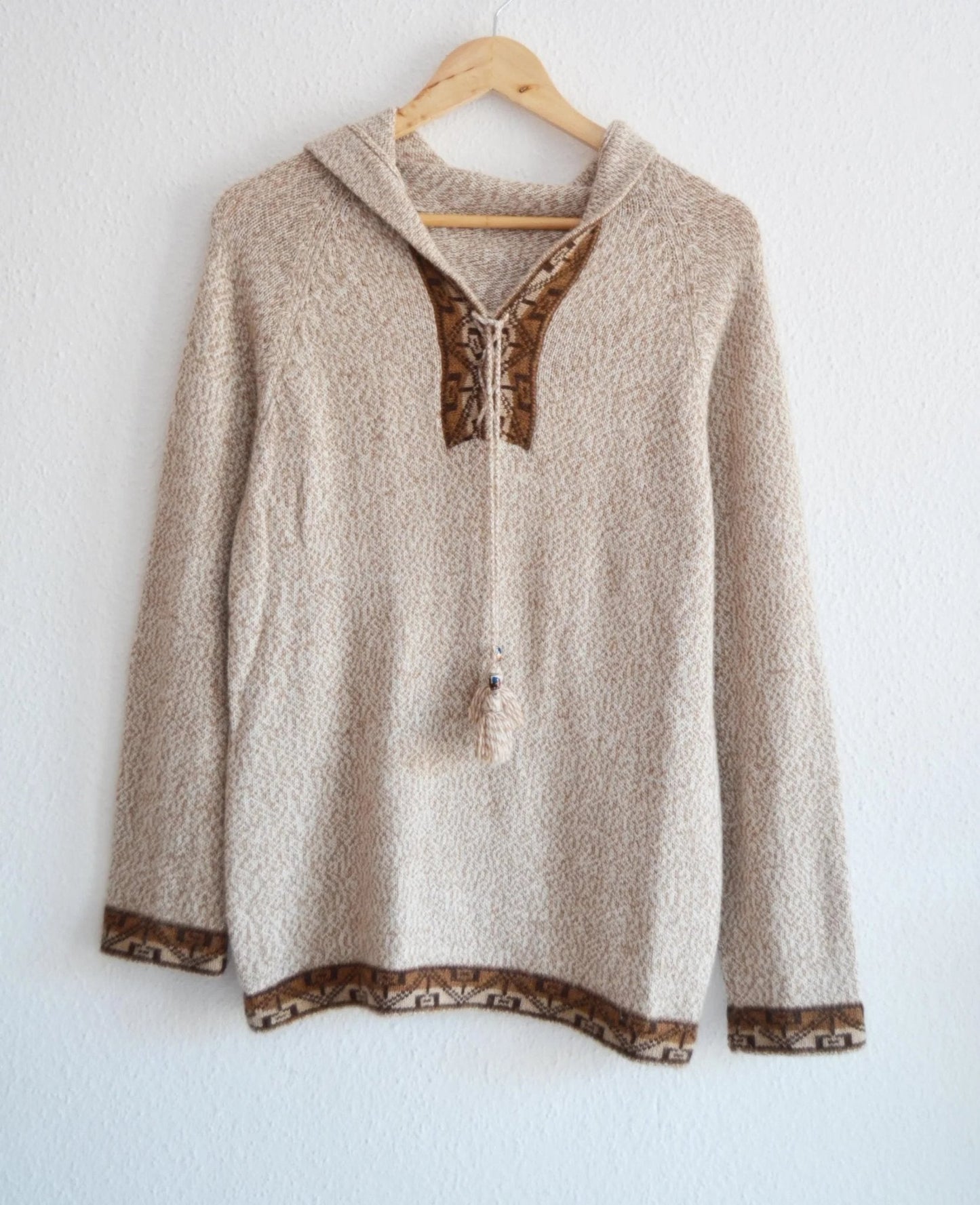 Handmade beige alpaca sweater with brown patterned trim and hood on wooden hanger.