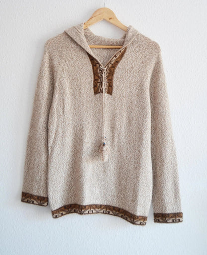 Handmade beige alpaca sweater with brown patterned trim and hood on wooden hanger.