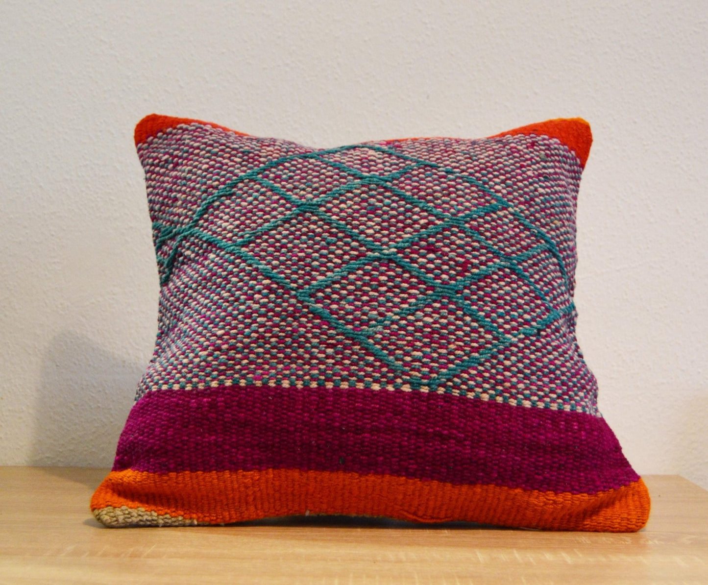 Handmade woven alpaca pillow with geometric patterns in magenta, orange, and green.
