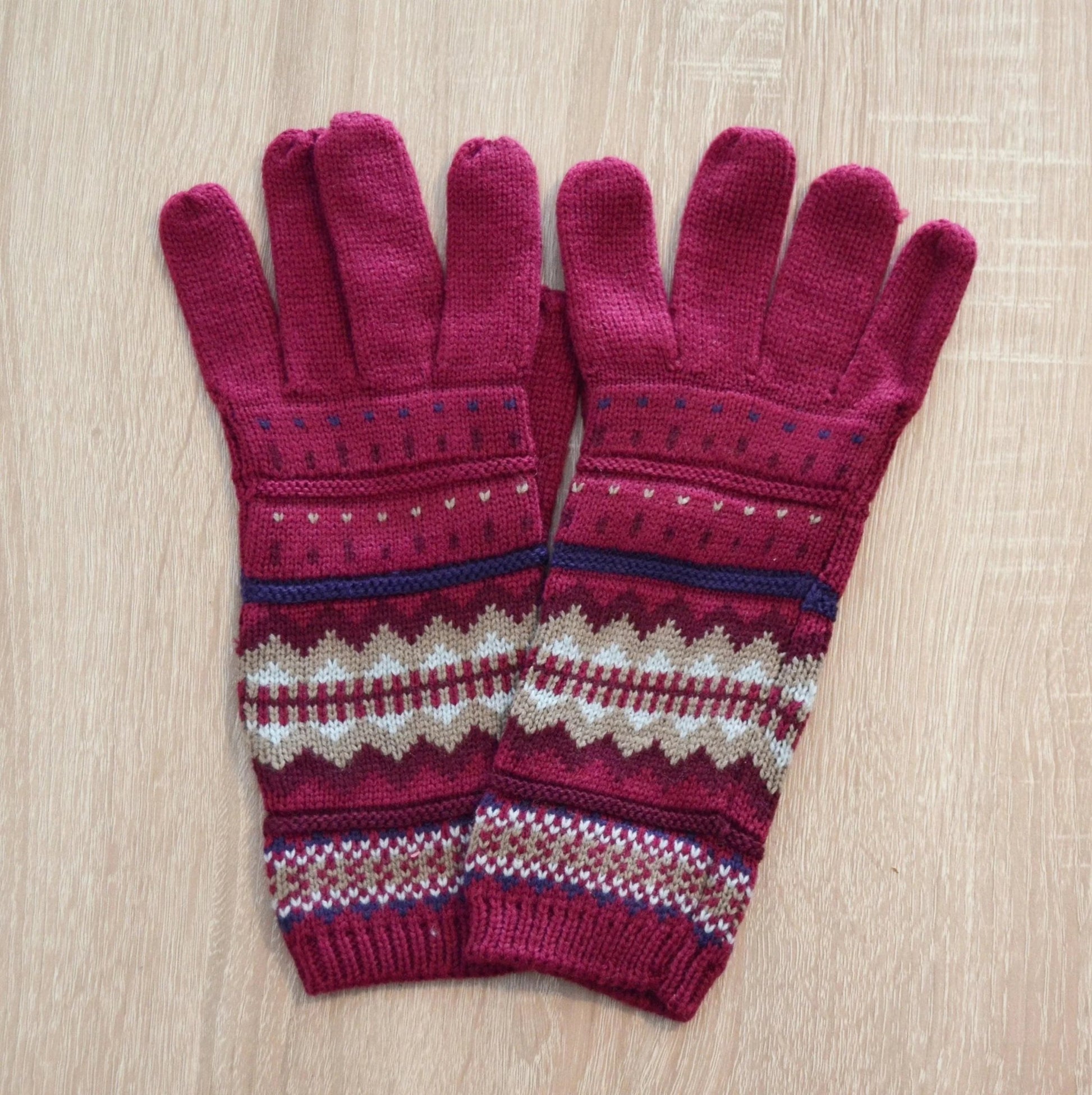 Handmade alpaca gloves in pink with geometric patterns and ribbed cuffs on wood background.