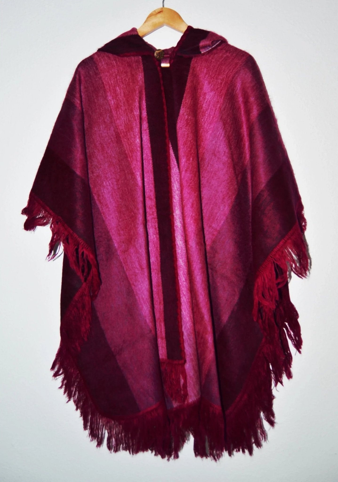 Handmade alpaca wool hooded poncho in rich burgundy with fringed edges and ethnic pattern accents.