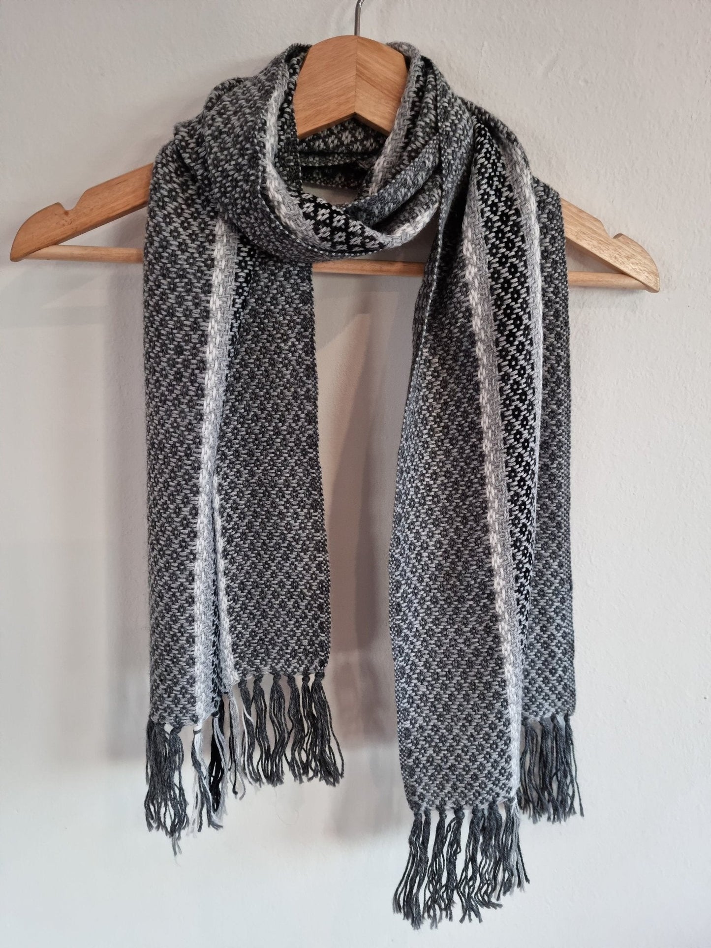 Handmade gray alpaca wool shawl with textured pattern and fringed ends hanging on wooden hanger.