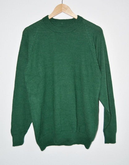 Handmade green alpaca wool sweater with long sleeves and crew neck hanging on wooden hanger.