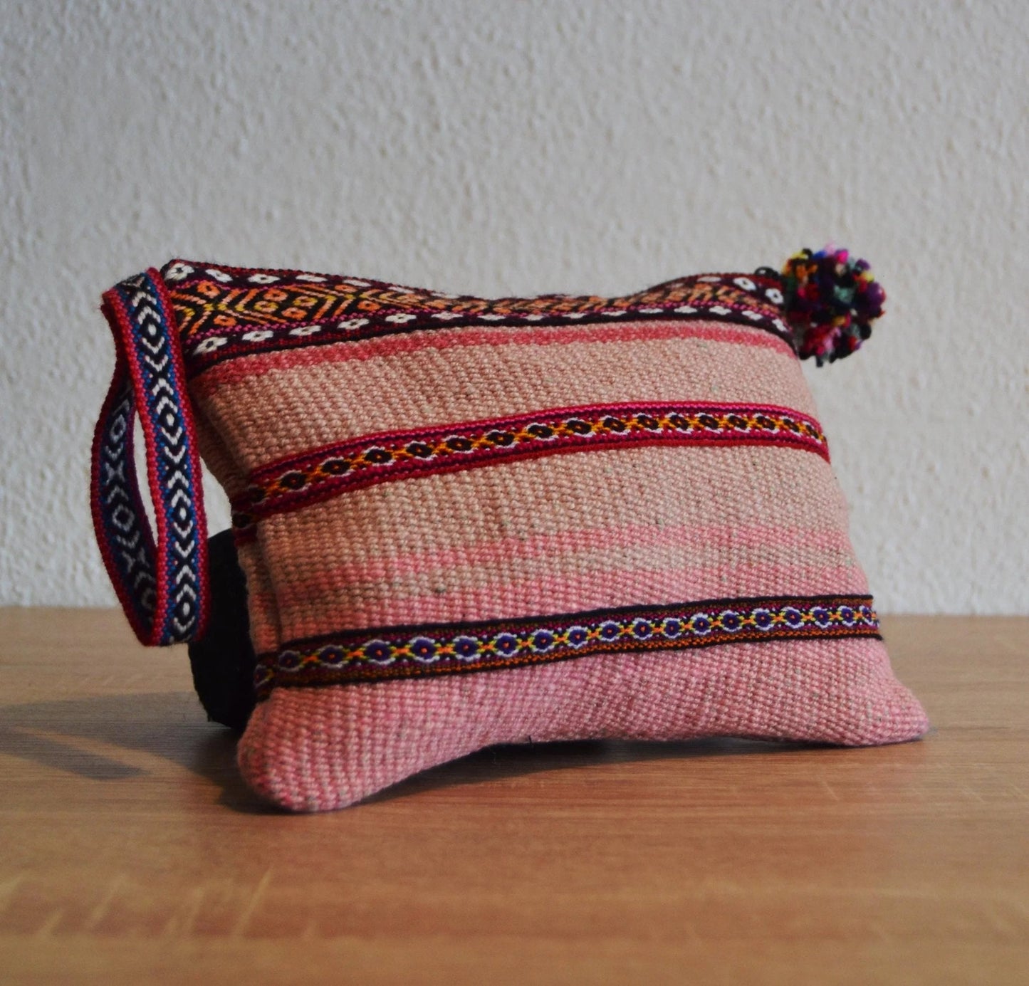 Small handmade alpaca coin purse in pink with colorful woven details and pom-pom zipper pull.