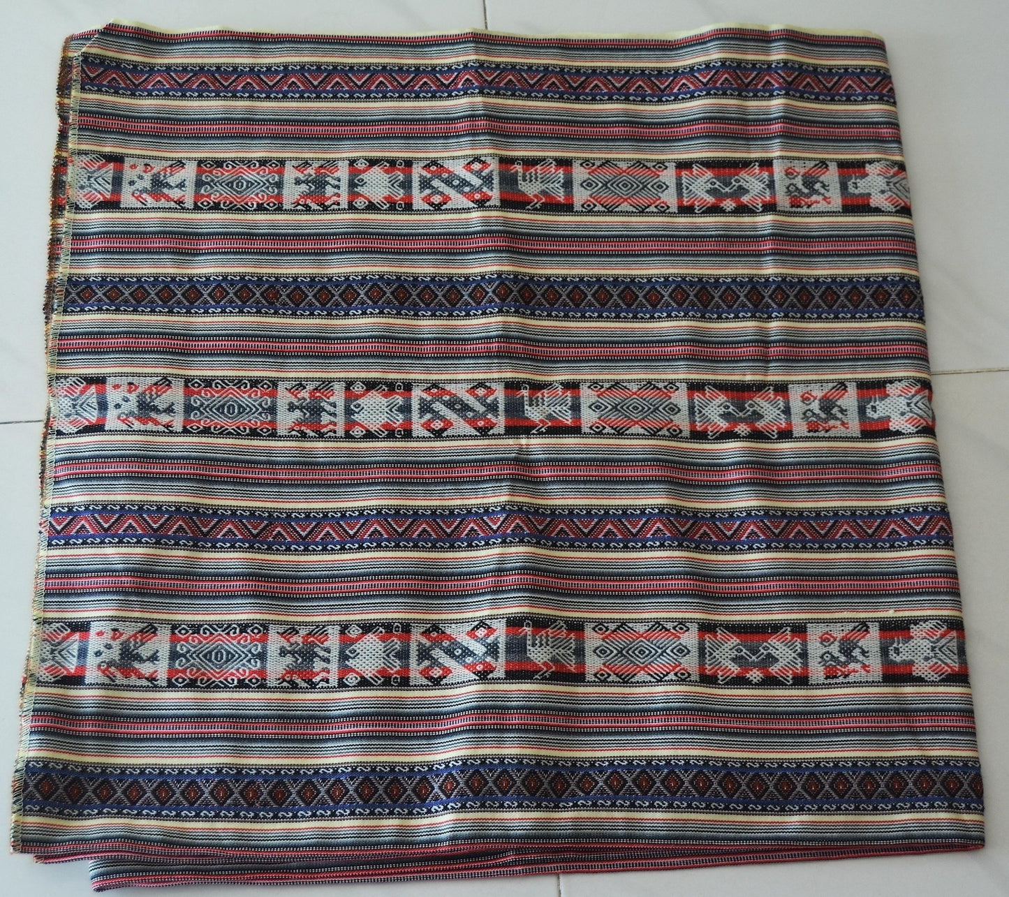 Handmade alpaca textile blanket with colorful geometric Andean patterns on cream background.