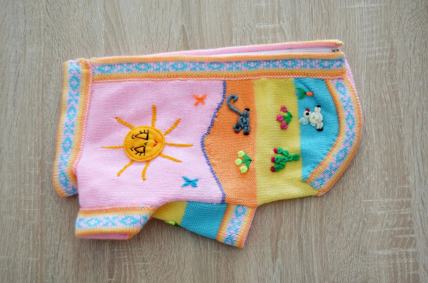 Handmade alpaca dog sweater with colorful sun and animal embroidery in pink, orange, yellow, and blue panels.