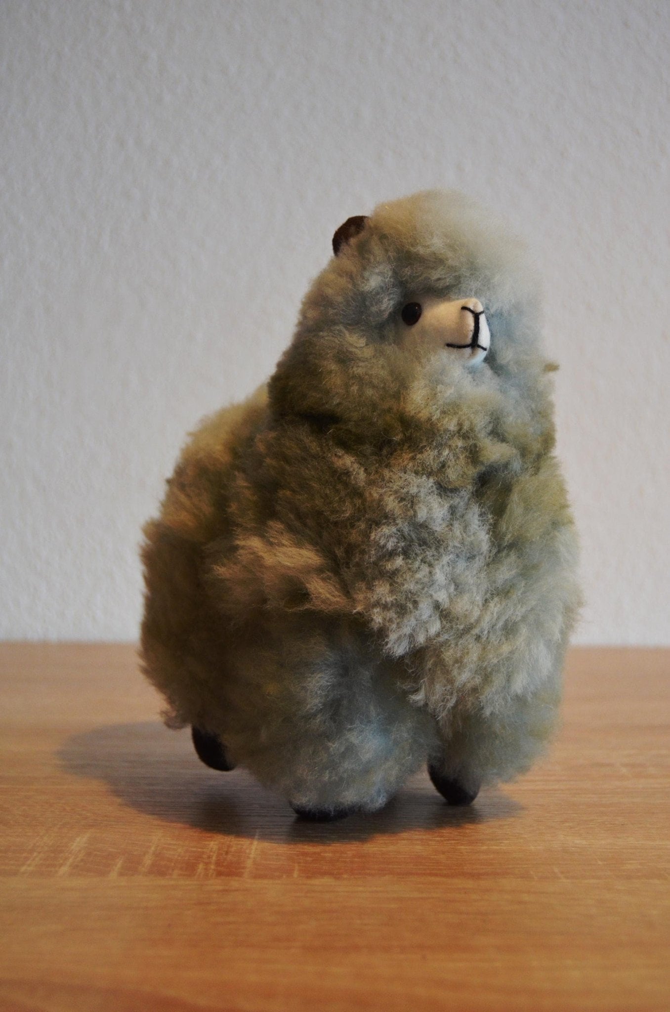 Small handmade brown alpaca plush with soft fluffy wool standing on wooden surface.