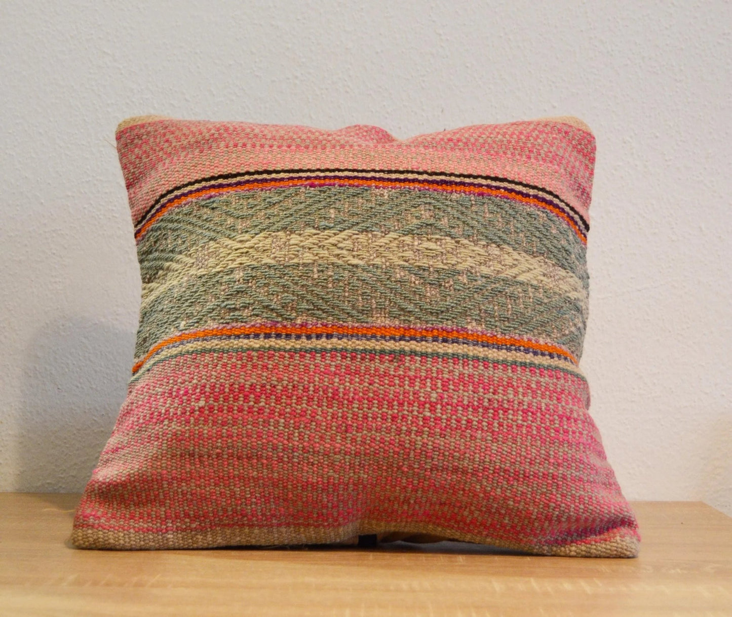 Handmade colorful woven alpaca pillow with ethnic patterns in pink and green tones.