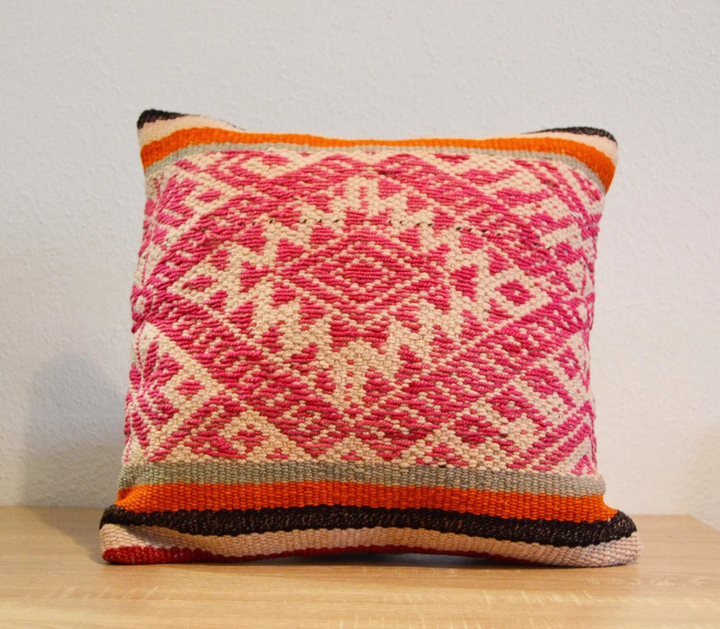Handmade Peruvian pillow with pink and beige alpaca woven geometric pattern and orange-striped border.