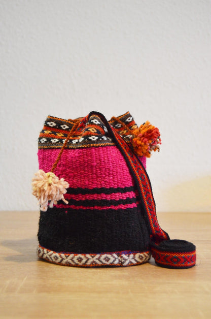 Handmade alpaca mini shoulder bag with bright pink, black, and orange geometric patterns and pom-pom accents.