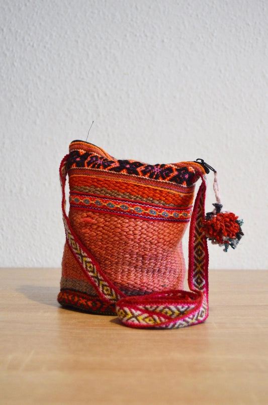 Handmade alpaca shoulder bag in vibrant red with traditional Andean patterns and pompom detail.