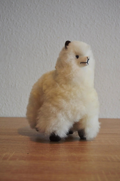 Handmade white alpaca plush with soft fluffy texture and black facial details on wooden surface.
