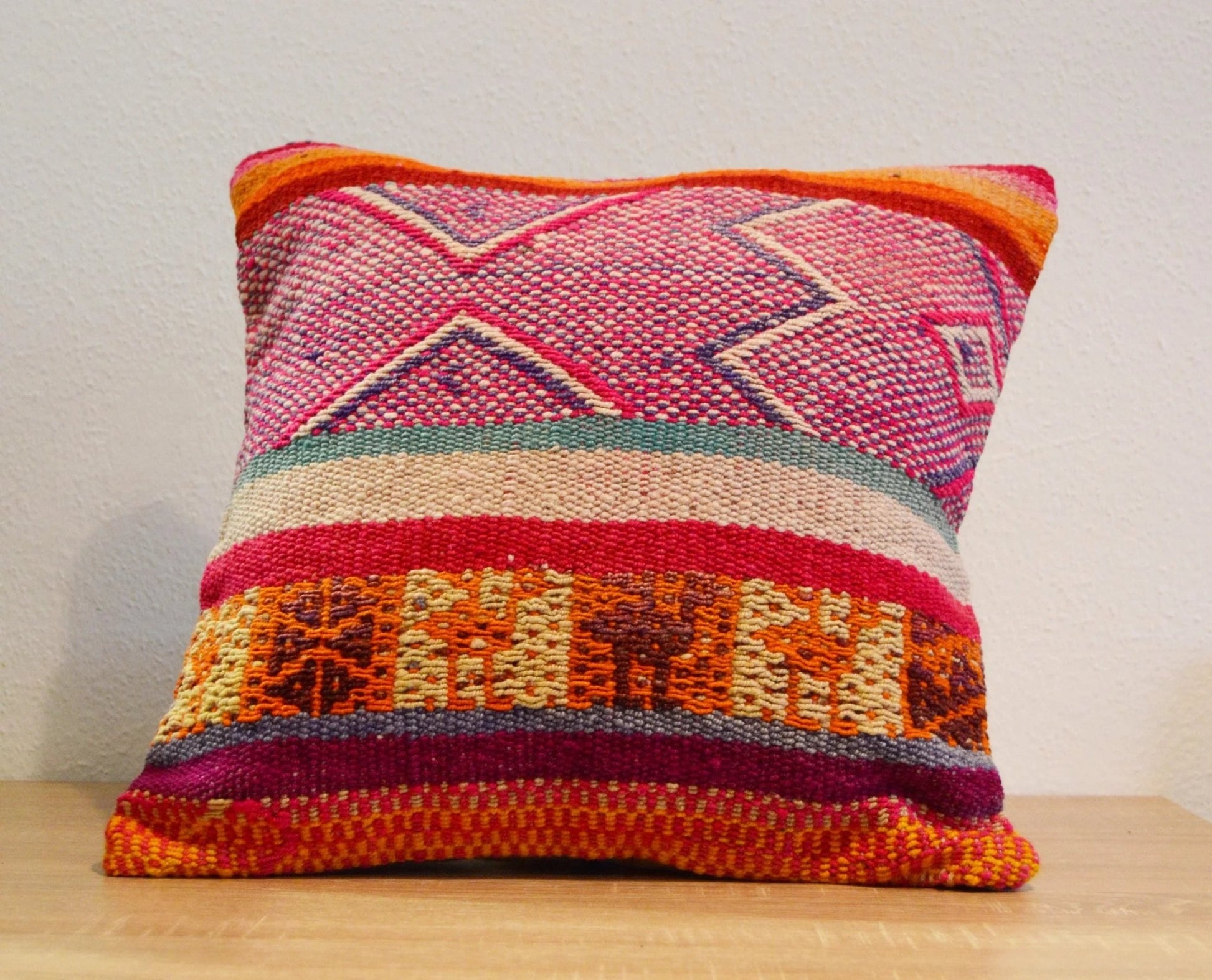 Handmade Peruvian pillow in vibrant pink, orange, and red woven alpaca with geometric patterns.