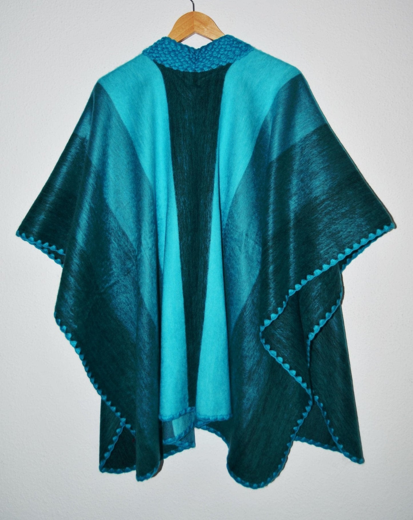 Handmade alpaca wool poncho shawl in turquoise and dark teal with geometric patterns and tasseled edges.