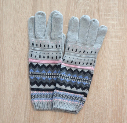 Gray handmade alpaca gloves with geometric blue, pink, and black patterns on wood background.
